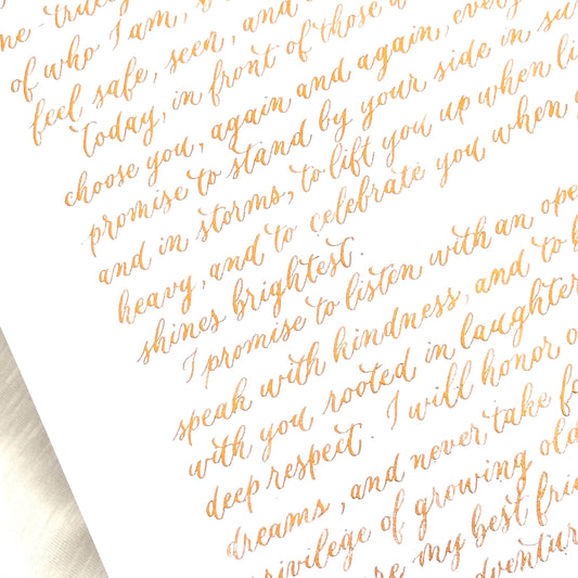 Handwritten close up of metallic gold calligraphy on white paper showing elegant flowing script herpens
