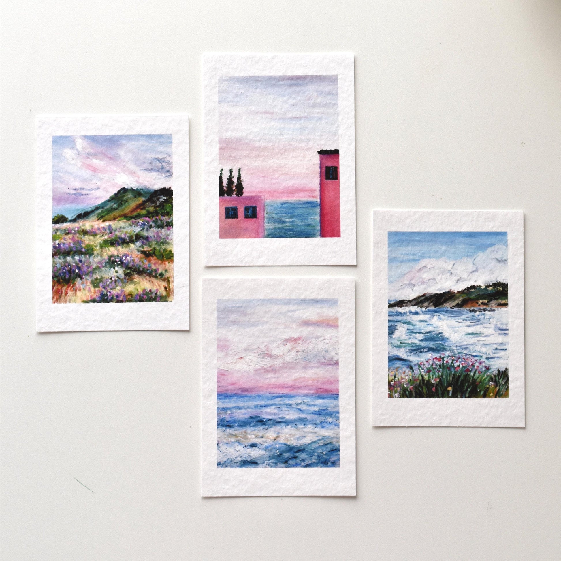 Set of four A6 oil pastel landscape postcards by HerPens — coastal waves, sunset sky, pink house by the sea, and wildflower field, printed on textured fine art paper.