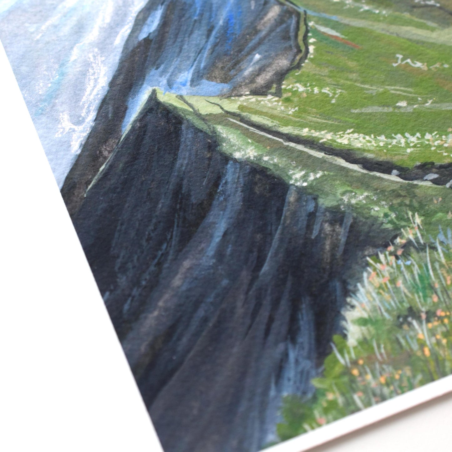 Close-up of the “Verdant Peaks” gouache painting — rocky dark cliff, green ridge, and tiny wildflowers, showing brush texture and print quality.