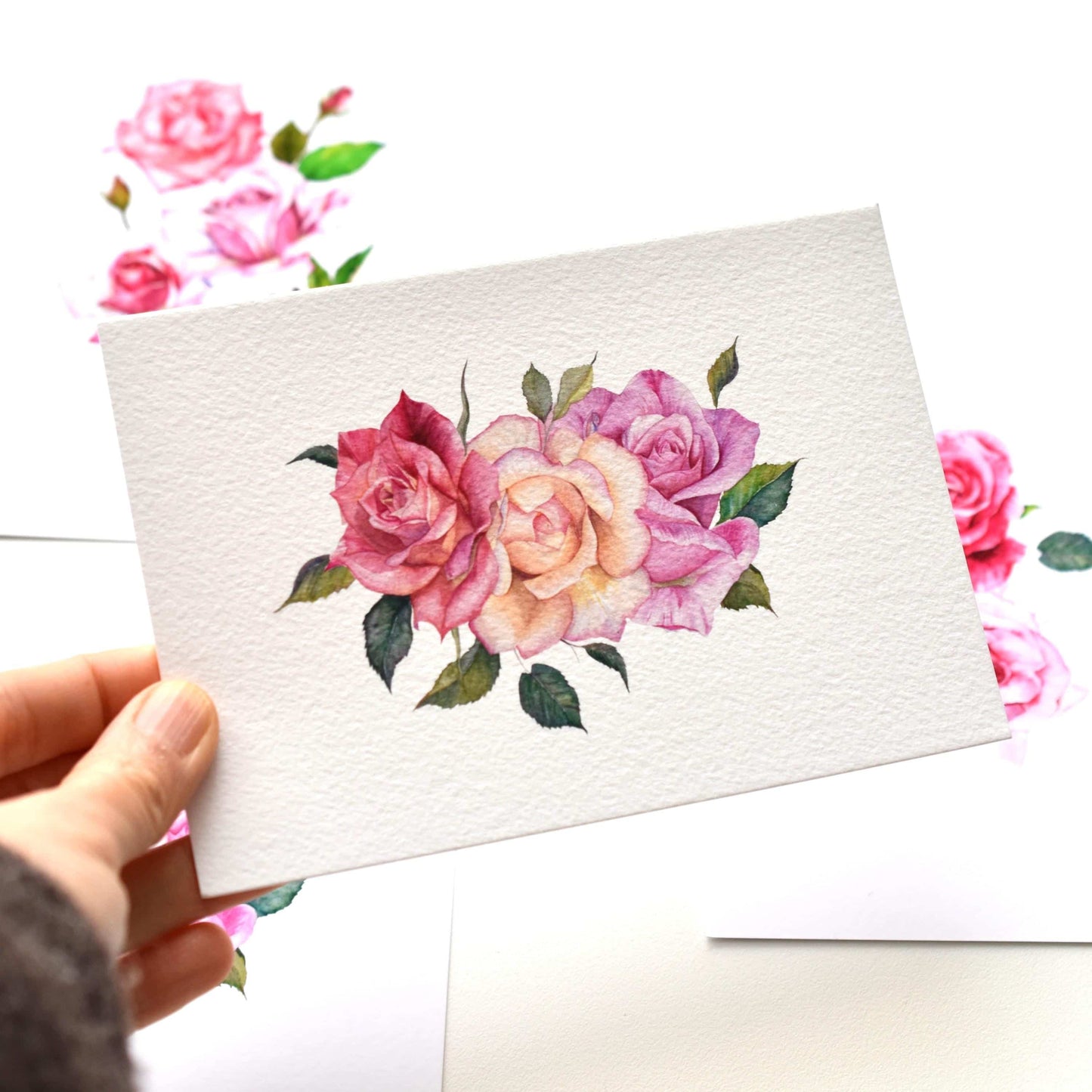 Handheld A6 watercolor roses postcard shown from an angled view, highlighting textured fine art paper and delicate floral illustration, HerPens