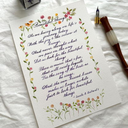 Handwritten calligraphy letter with watercolor floral border and dip pen beside it