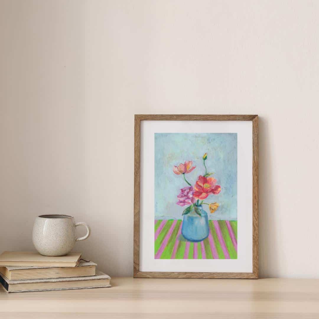 Framed artwork of flowers in a vase on a table with books and a mug.