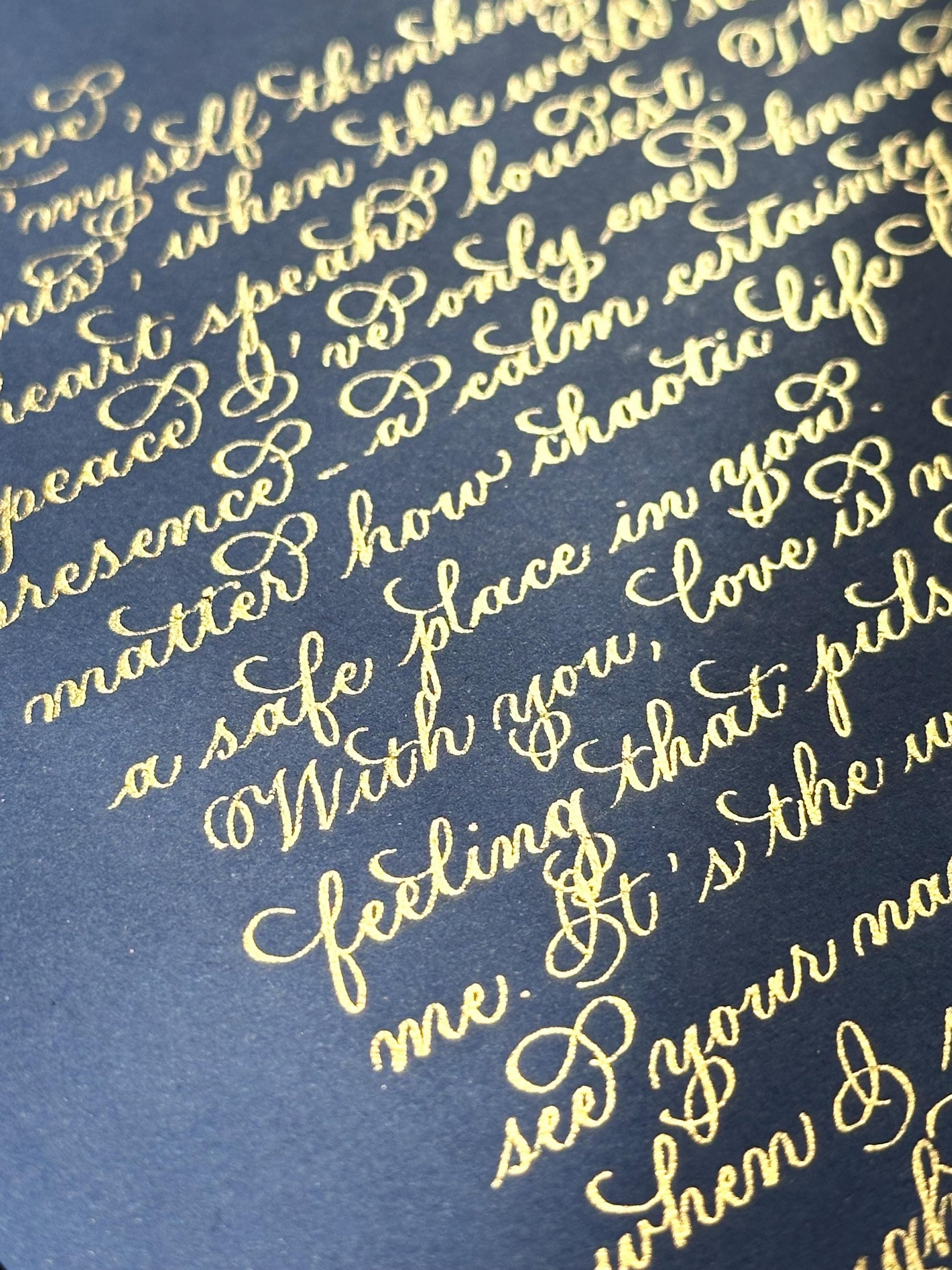 Handwritten close up of gold ink calligraphy on navy paper showing detailed flourishing script herpens
