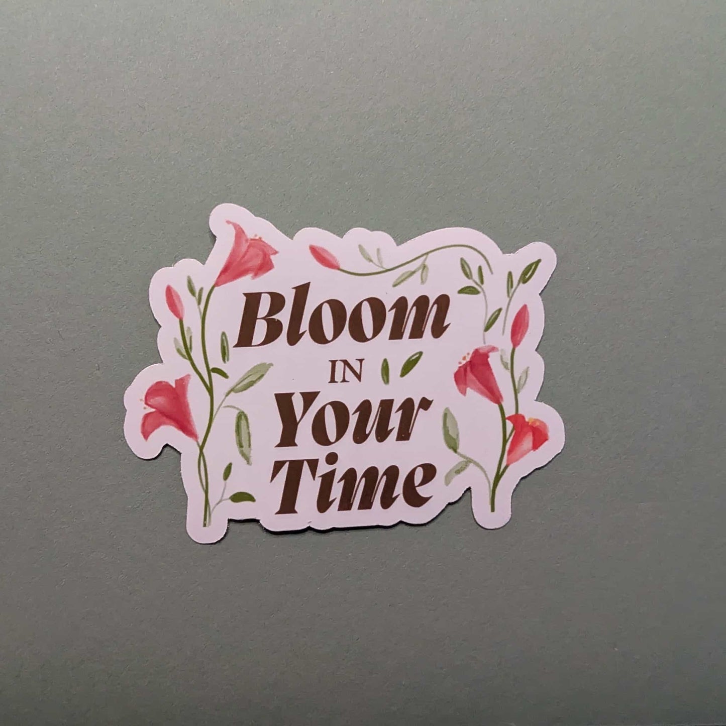 Sticker with 'Bloom In Your Time' text on a gray background