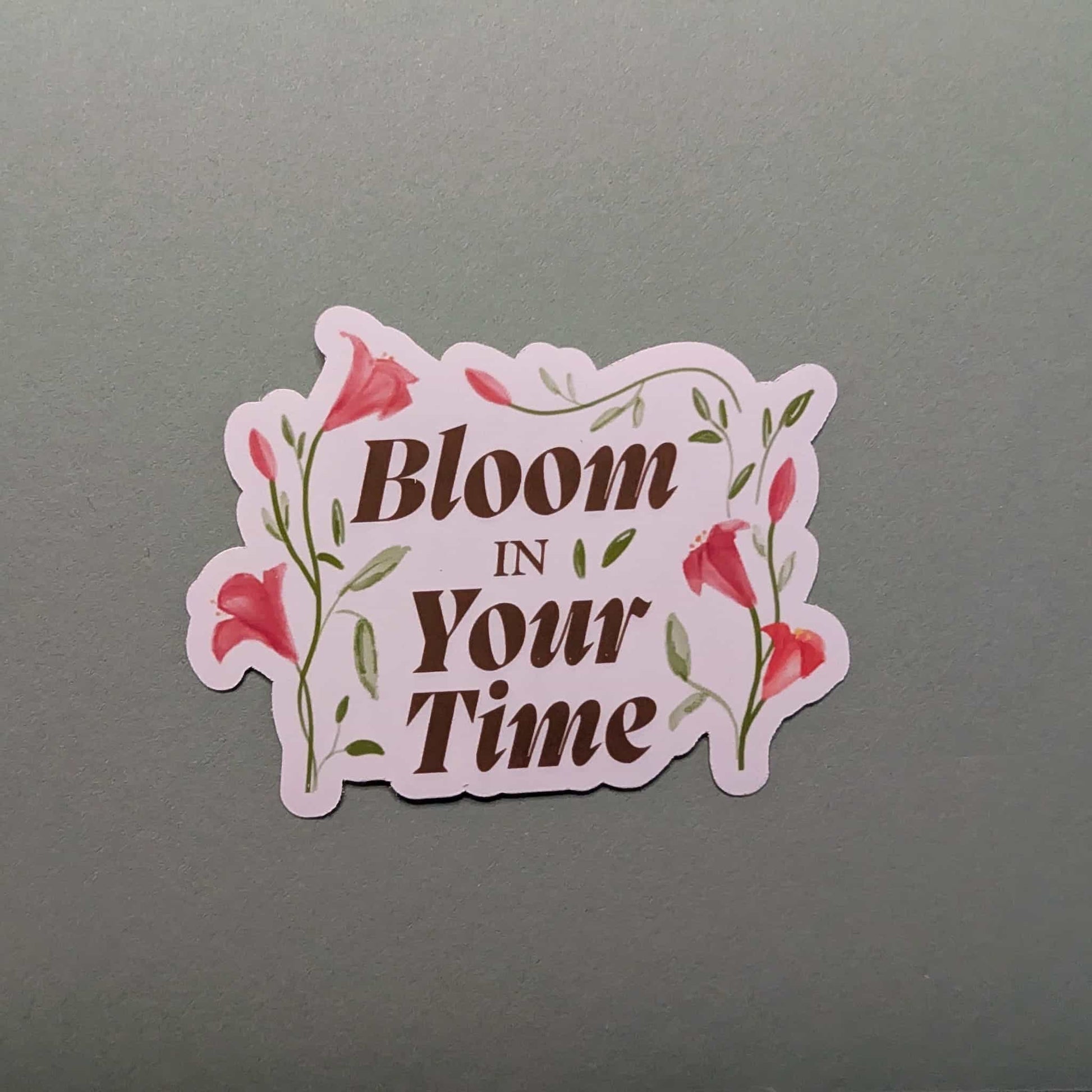 Sticker with 'Bloom In Your Time' text on a gray background