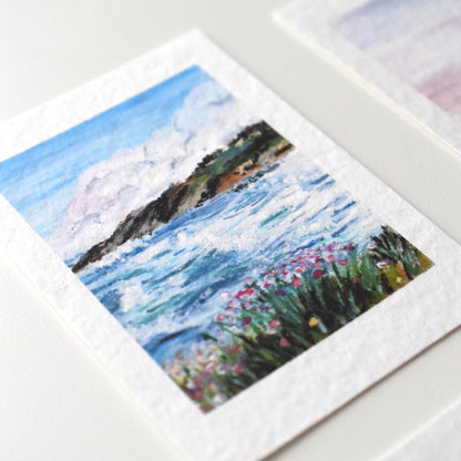 A6 oil pastel postcard of a windy coastal scene with crashing waves, wild coastal flowers, and distant cliffs — printed on textured fine art paper by HerPens.