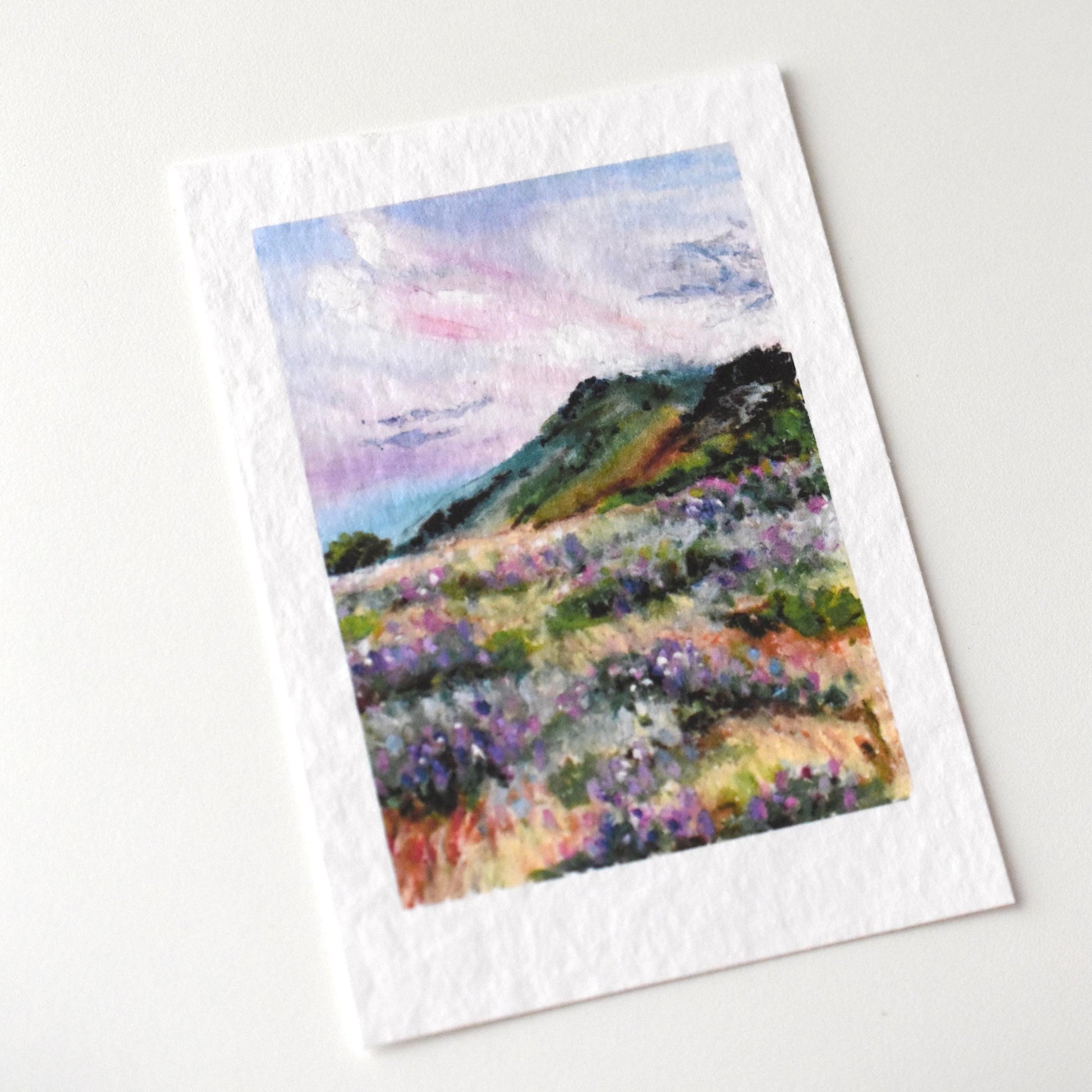 A6 oil pastel postcard of a wildflower meadow on a hillside under a soft evening sky — printed on textured fine art paper by HerPens.