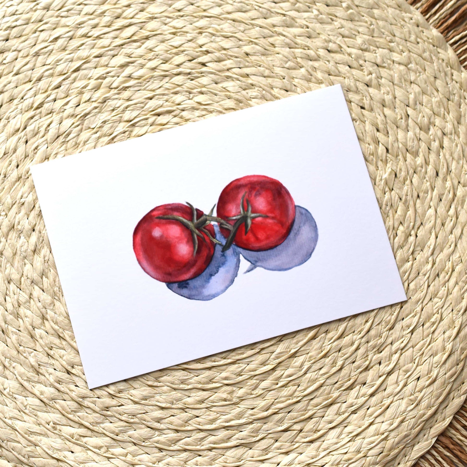 Art print of red tomatoes on a white background, placed on a woven mat.