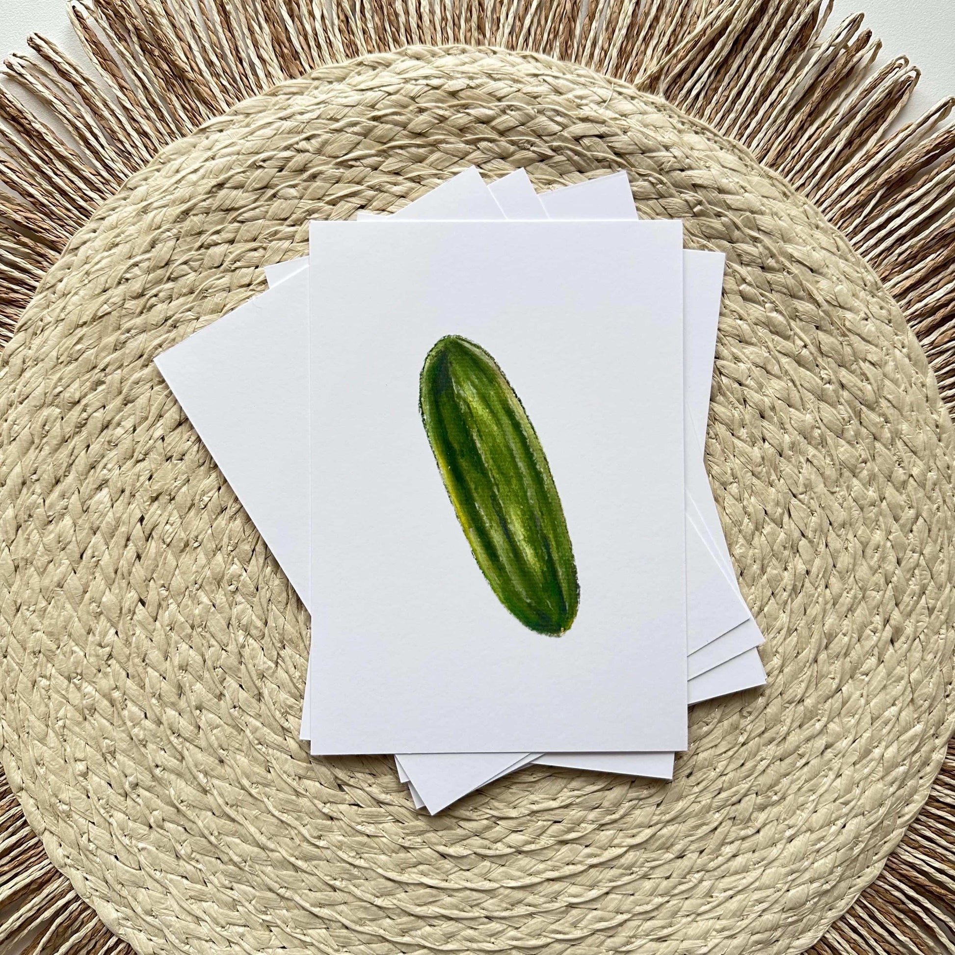 Stack of greeting cards with a cucumber illustration on a woven mat