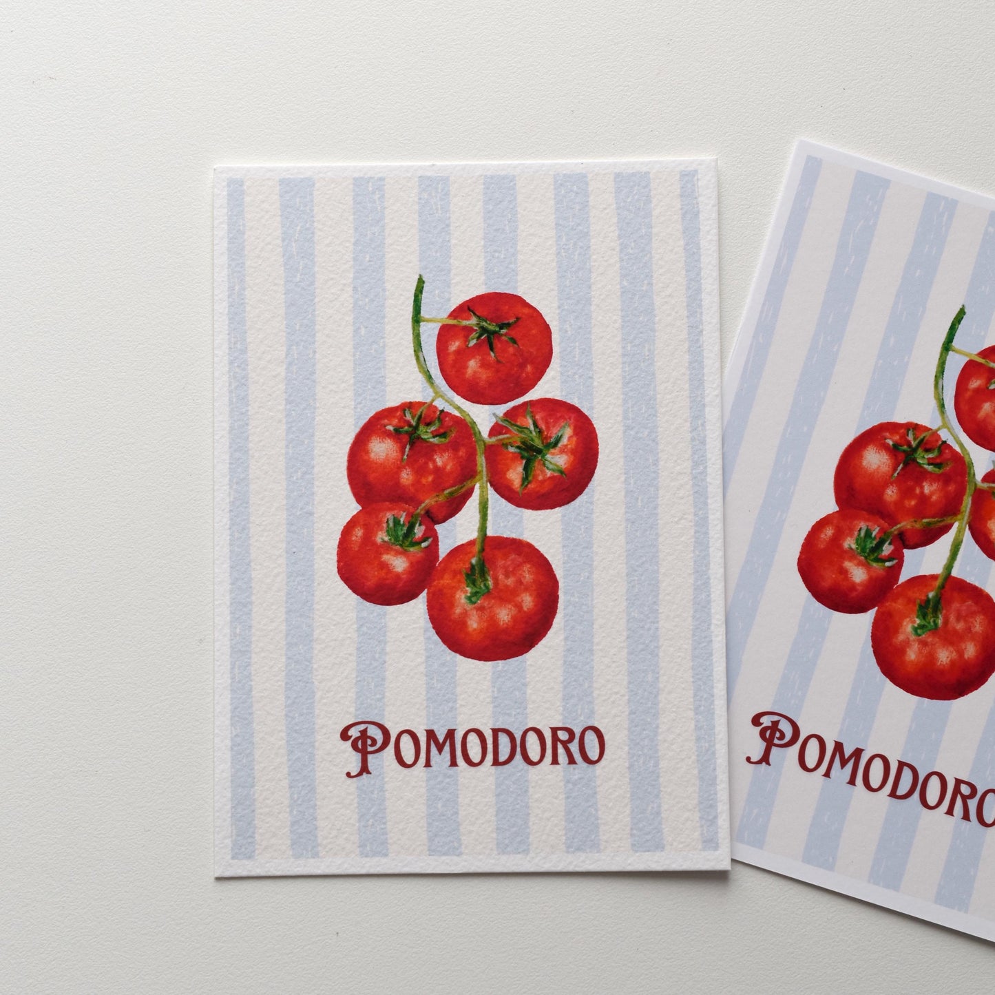 “Pomodoro” A6 postcard — tomatoes illustration on soft blue stripes, printed on textured fine art paper with visible painterly surface, by HerPens.