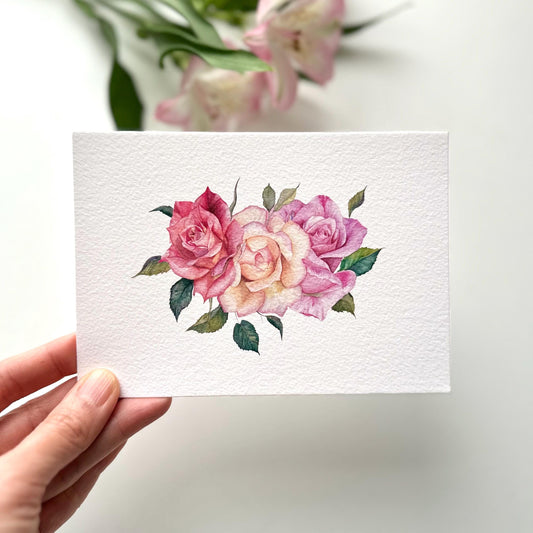 Hand holding A6 watercolor roses postcard printed on textured fine art paper, soft floral illustration with gentle rose details, HerPens