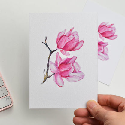 “Watercolour Magnolia” A6 art printed postcard held in hand — delicate magnolia bloom on fine art paper, by HerPens.
