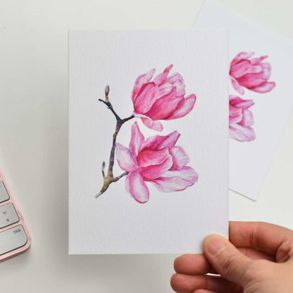 Hand holding a card with pink floral design on a white background