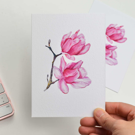 Hand holding a card with pink floral design on a white background